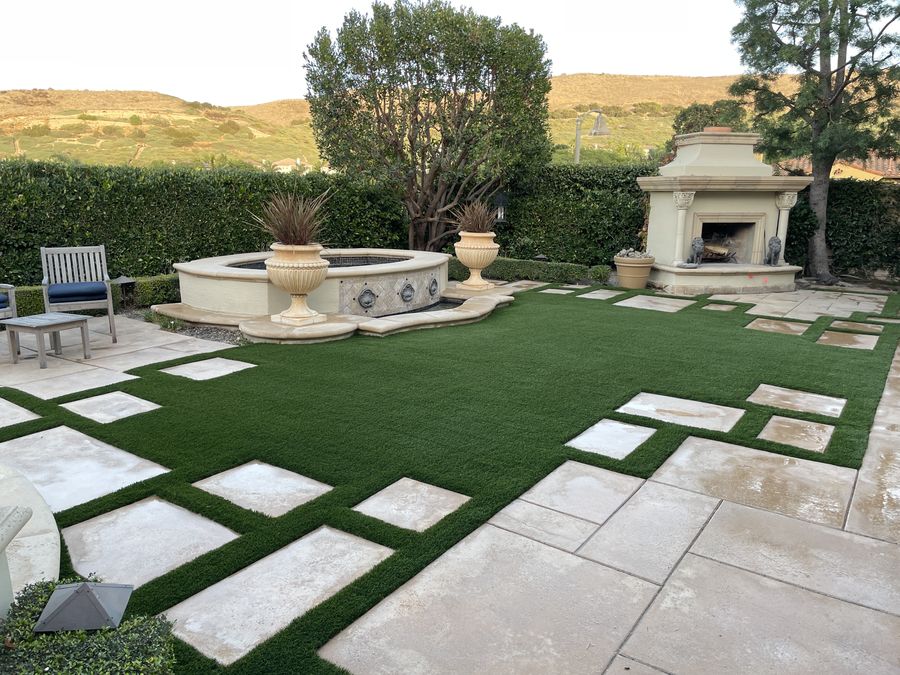 Paver squares set into turf, leading to a stone fountain and fireplace
