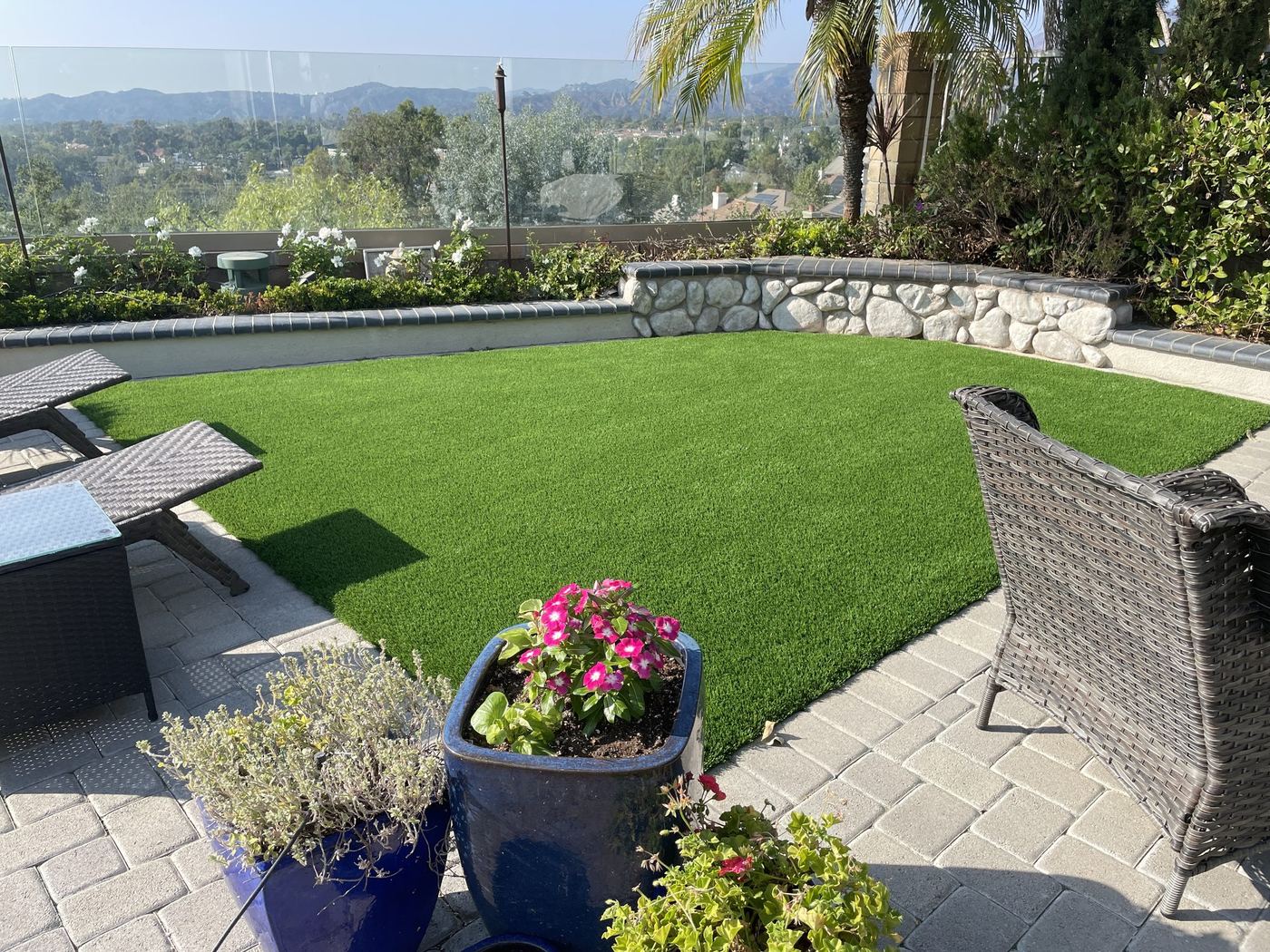 Backyard lawn edged with pavers, patio seating and a hillside view